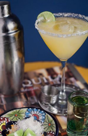 Gold Margarita next to a cocktail shaker and a tequila shot